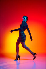 Fototapeta na wymiar Full lenght photo of running woman, young fashion model wearing fashionable in transparent top and skirt posing over gradient yellow-red neon background.