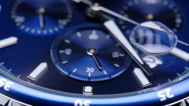 second hand ticking on a blue watch face. Men's chronograph watch in metal with sapphire crystal. closeup view of rotating watch, running second arrow. blue dial
