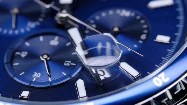 second hand ticking on a blue watch face. Men's chronograph watch in metal with sapphire crystal. closeup view of rotating watch, running second arrow. blue dial