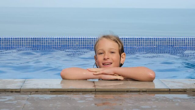 Portrait of little girl enjoying bathing in infinity pool over beautiful blue sea, slow motion. Summer vacation and travel concept