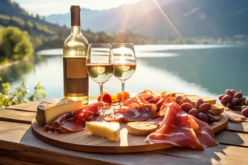 Rolgordijnen Italian appetizer prosciutto antipasti and and wine on a wooden terrace overlooking mountain lake.  © colnihko