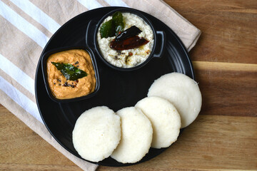Idli and chutney in a black plate on wooden board. South Indian idlis.