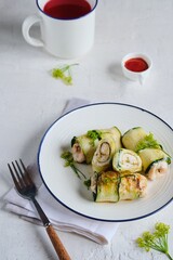 Fried chicken rolls wrapped with sliced zucchini on a white plate on a light concrete background. Recipes for zucchini.