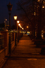 Fototapeta na wymiar Long narrow path next to river with a lot of glowing city lamps at dark afternoon
