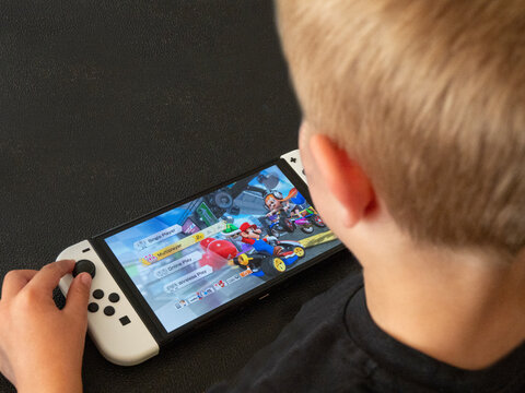 Young boy playing Mario Kart on a popular new Nintendo Switch console in handheld mode. Close up image on hands. Copenhagen, Denmark - August 5, 2023.