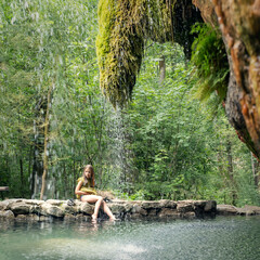 Young girl sitting in a forest near a natural waterfall in Europe, Luxembourg. 