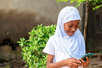 African school girl in a white hijab looking at a cell phone