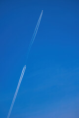 Race of two commercial airplanes at cruising altitude in blue sky with long contrails. 