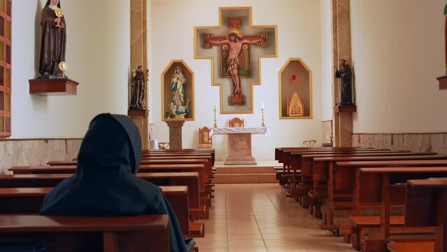 Fraile monje sacerdote padre Franciscano sentado leyendo meditando orando la Palabra de Dios en la Biblia en capilla iglesia Templo Católico cristiano con Jesús crucificado en la cruz 
