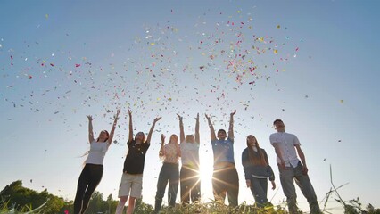 Friends toss colorful paper confetti from their hands against the rays of the evening sun.