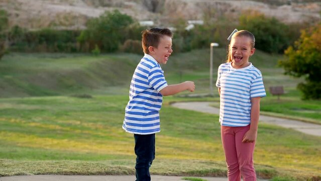 Ni&ntilde;os hermanos amigos primos felices jugando divertidos alegres en parque del vecindario en verano en vacaciones al aire libre riendo y disfrutando de su amistad al atardecer vestidos de rayas 