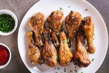Closeup of baked chicken drumsticks with green onions and sesame seeds on a plate top view