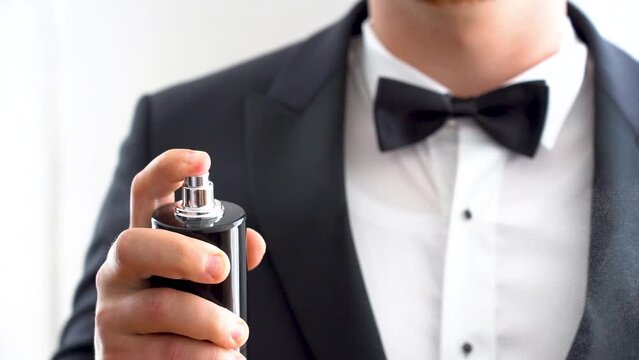 Mężczyzna w smokingu i muszce używa perfumu. Mgiełka z dozownika perfumu