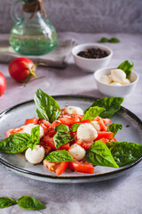 Caprese salad with tomatoes, mozzarella, basil and olive oil on a plate vertical view