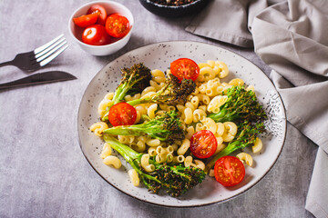 Salad of pasta, tomatoes and fried broccoli sprouts on a plate on the table