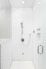 A walk-in shower with white wavy tiles on the walls, chrome faucet, and circular tile floor.