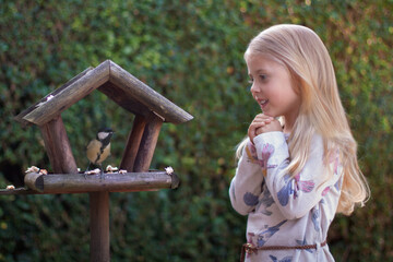 Adorable kid looking at a great tit in a bird feeder house which eats bread