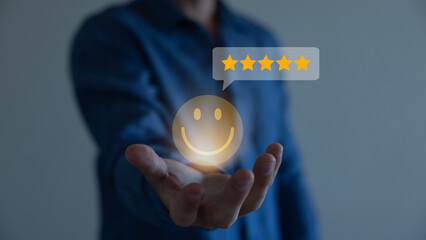 Businessman using a mobile phone to point to a smile face and five stars icon, representing...