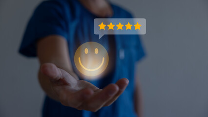 Businessman using a mobile phone to point to a smile face and five stars icon, representing...