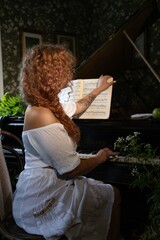Turning the pages of music, a girl near the piano sits on a chair