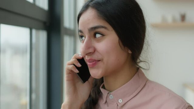 Cheerful laughing Indian Arabian girl gen z student speak mobile phone at office casual carefree conversation happy female businesswoman woman sharing news talk cellphone call communicate with friend
