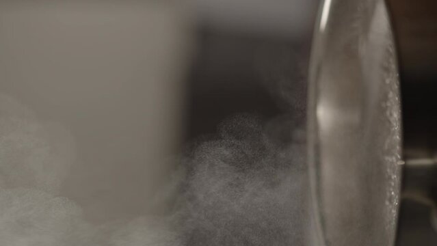 Slow motion vertical shot of steam rising from steel saucepan on stove