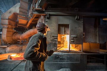 Steelworker at work near arc furnace and pouring liquid metal  - 631627422