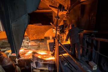Steelworker at work near arc furnace and pouring liquid metal  - 631627426
