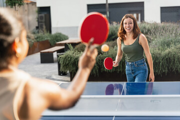 Happy girl friends playing ping pong table tennis, having fun together at the University campus  - obrazy, fototapety, plakaty