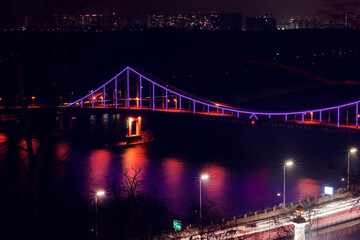 Night city minimal landscape. Dark and tranquil long exposure photography with led illuminated bridge and light reflections in the water. Bridge across the Dnipro river, Kyiv, Ukraine