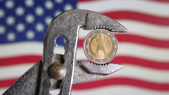 German Euro Coin with Federal Eagle in Pliers Against US Flag Background as Symbol of Economic Sanctions