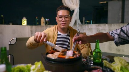 Group of Diversity Asian people friends enjoy and fun celebration meeting dinner party eating barbecue grill and drinking Korean vodka together at outdoor rooftop on summer holiday vacation at night.