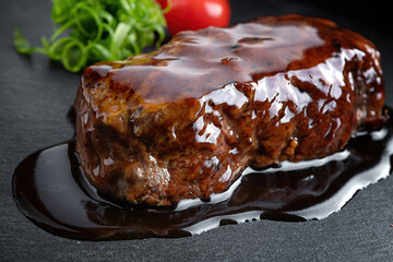 Pork steak in teriyaki sauce on a black stone. Close-up