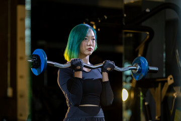 Asian woman is practice weight lifing using easy bar as beginner on barbell for arm and core muscle inside gym with dark background for exercising and workout concept