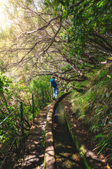 Tourist walking along a water canal path overgrown with trees on a sunny day. 25 Fontes Waterfalls, Madeira Island, Portugal, Europe.