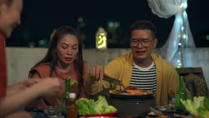 Group of Diversity Asian people friends enjoy and fun celebration meeting dinner party eating barbecue grill and drinking Korean vodka together at outdoor rooftop on summer holiday vacation at night.