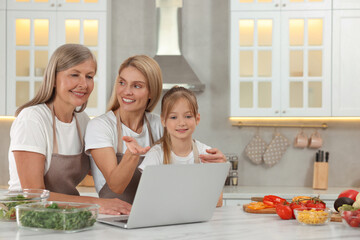 Three generations. Happy grandmother, her daughter and granddaughter using laptop in kitchen