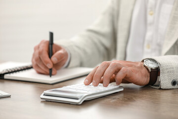 Fototapeta premium Professional accountant using calculator at wooden desk, closeup