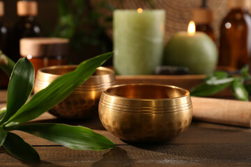 Green branch, singing bowls and burning candles on wooden table, closeup