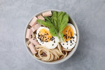 Bowl of delicious ramen with meat and egg on light grey table, top view. Noodle soup