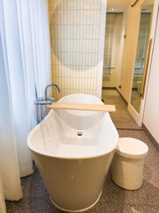 White bathtub with warm lighting against with hot and cold water faucet and wooden plaque for storage