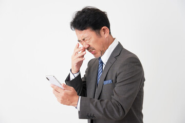 スマートフォンを持って悩むミドルエイジのビジネスマン　白背景