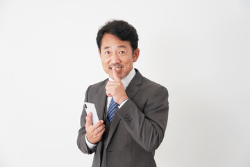 スマートフォンを持って内緒のポーズをするミドルエイジのビジネスマン　白背景