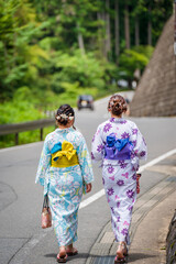 Back view of two women wearing Japanese yukata summer kimono walking on the road in nature of Kyoto, Japan.