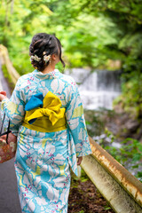 Back view of one woman wearing Japanese yukata summer kimono standing next to a river in Kyoto nature forest. Kyoto, Japan.