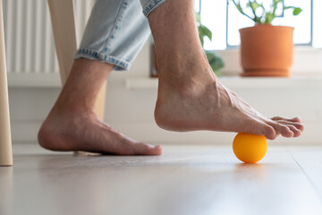Man using ball to relieve symptoms of arthritis in foot, close up. Person sitting on chair at home...