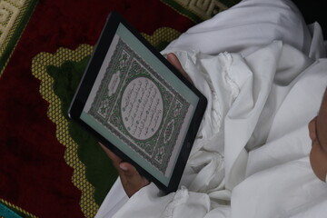 Muslim girl reading electronic Quran on tablet
