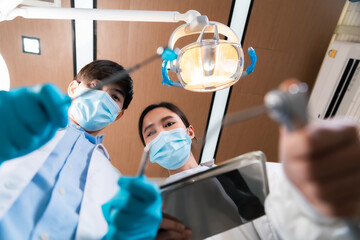 Asian female dentist adjusting surgical light looking from above at patient.