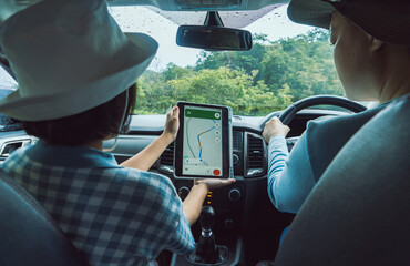 An Asian mother and daughter plan a trip in their car using an online satellite navigation system on a large tablet screen.