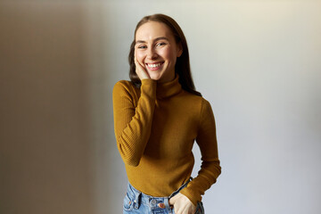Studio portrait of pretty young female student in yellow turtleneck and denim jeans posing against...